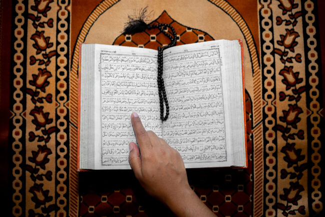 Muslim woman reading the Holy Quran using the finger. The Holy Quran on the mat of prayers . Top angle views. Indoors.